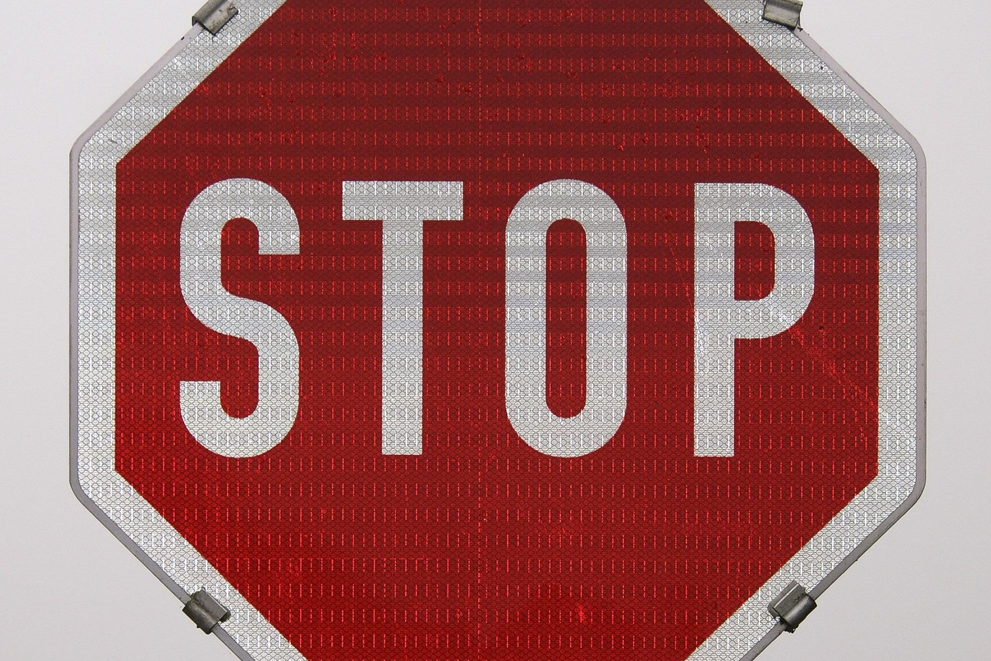 Rotes Stopschild mit weißer Schrift auf grauem Hintergrund.