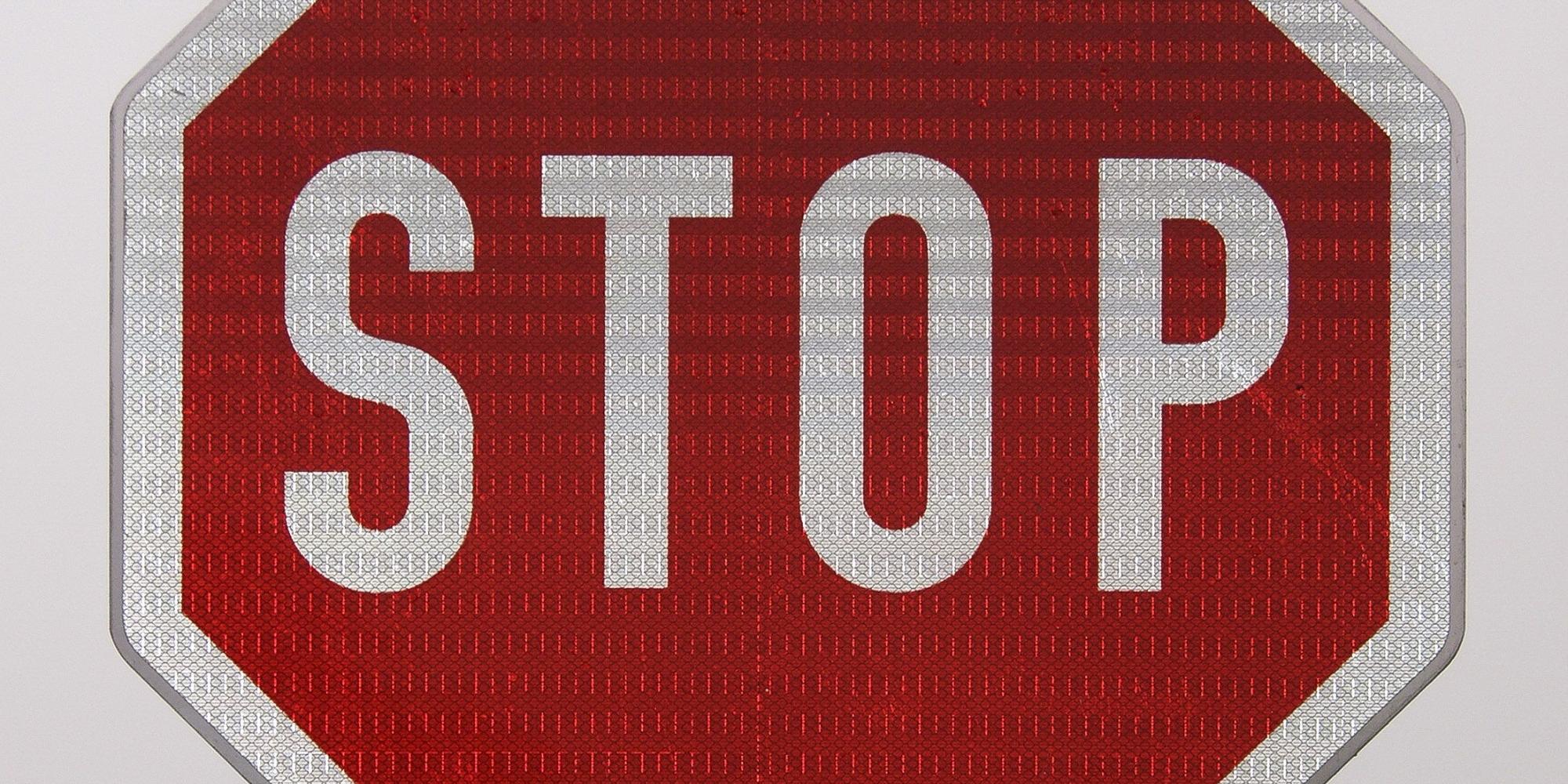 Rotes Stopschild mit weißer Schrift auf grauem Hintergrund.
