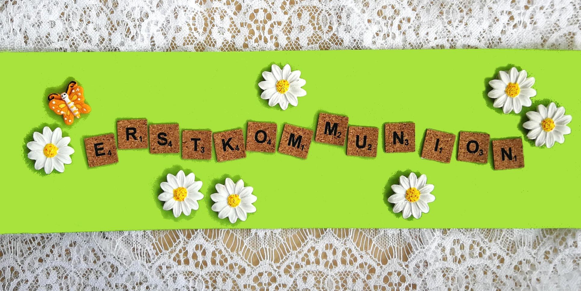 Holzbuchstaben „Erstkommunion“ auf grünem Hintergrund, umgeben von Gänseblümchen und Schmetterling.